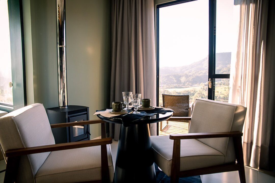 A room with a round table, two chairs, a small black table, and a view of the outdoors.