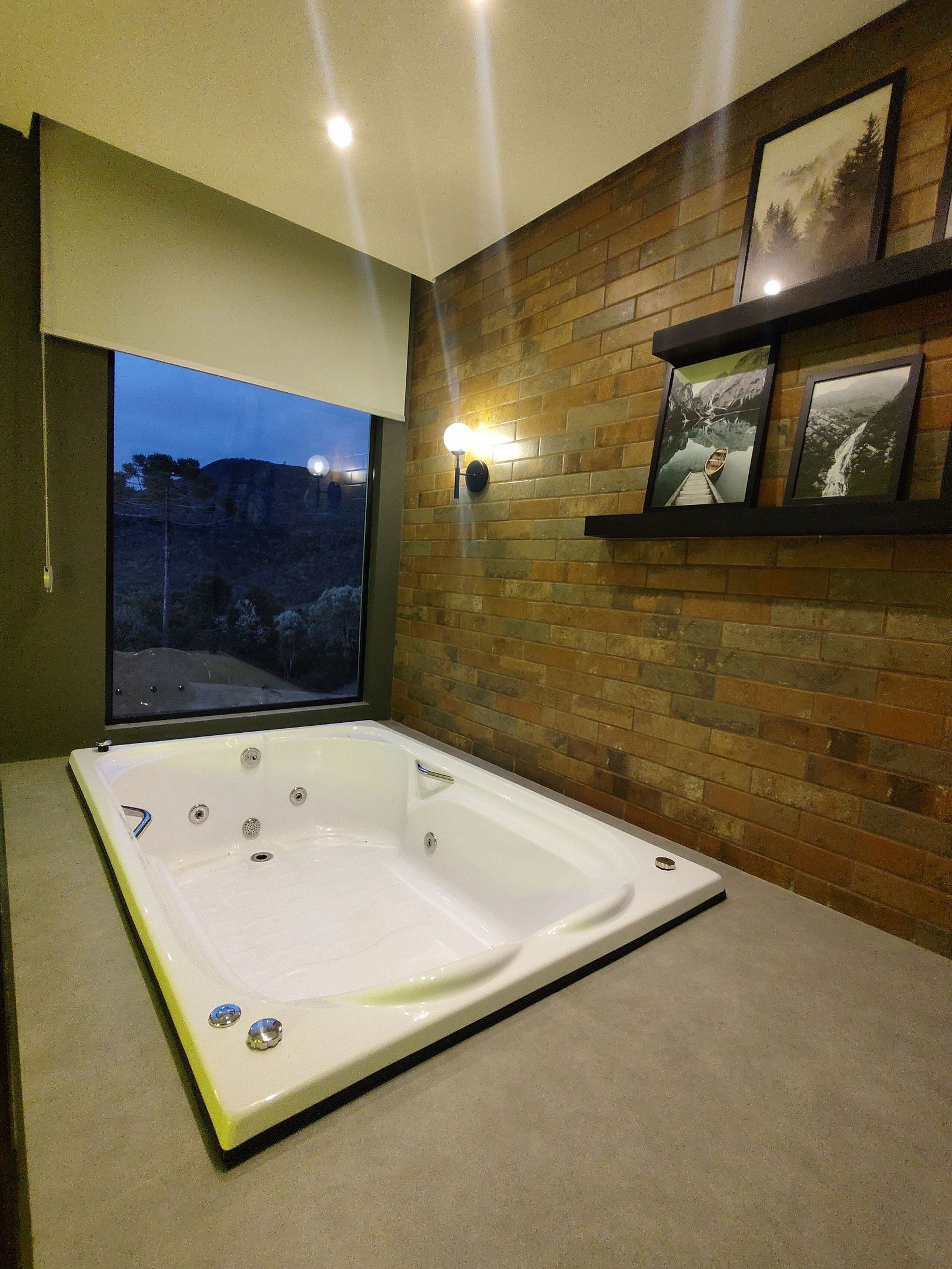 A modern bathroom with a large bathtub, a brick wall, and framed pictures.