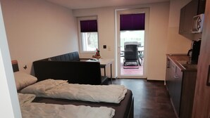 Ein kleines Zimmer mit Bett, einem Tisch, einem Stuhl und einer Küchenzeile.