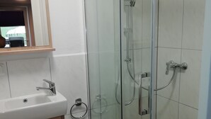Ein Badezimmer mit einer Duschkabine, einem Waschbecken mit Spiegel darüber und Holzschränken.