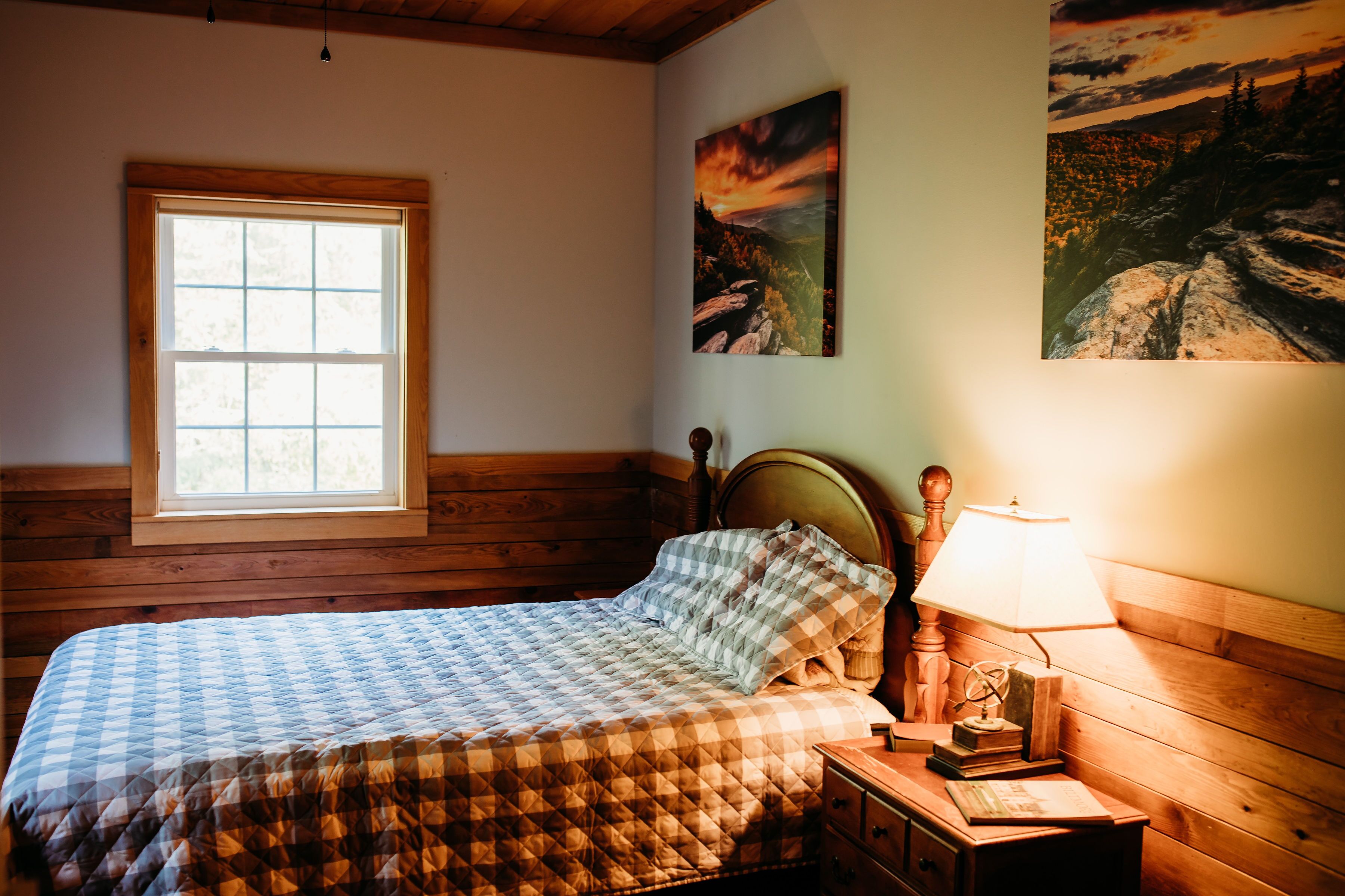 Une chambre à coucher avec un lit en bois, une fenêtre et deux tableaux accrochés au mur.