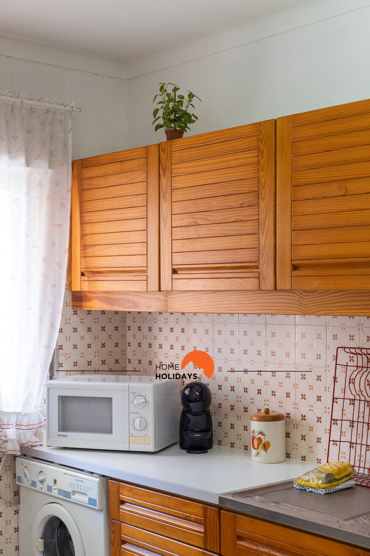 A compact kitchen with wooden cabinets, a microwave, a coffee maker, and a washing machine.