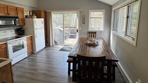 Une cuisine avec des meubles en bois, une table à manger et une porte-fenêtre coulissante donnant sur une terrasse.