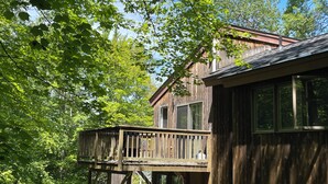 Une cabane en bois rustique, dotée d’une terrasse et de grandes fenêtres, entourée d’un feuillage verdoyant et luxuriant.