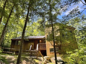 A rustic cabin surrounded by tall trees, featuring a wooden deck and a staircase leading to the entrance. - The Cabin at Crown Ridge, Nestled in the White Mountains of New Hampshire (Conway)