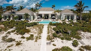 A beachfront property with a central pool, multiple lounge areas, and a symmetrical architectural design. - Beachfront Villa w/ Infinity Pool & Chef (Long Bay)