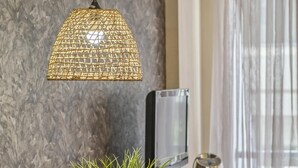 Een eethoek met een glazen tafel, geweven lampenkappen, een geweven plantenpot en een televisie op een houten kast.