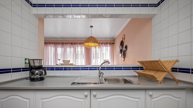Een keuken met witte kasten, een spoelbak, een koffiezetapparaat en een hangende lamp.