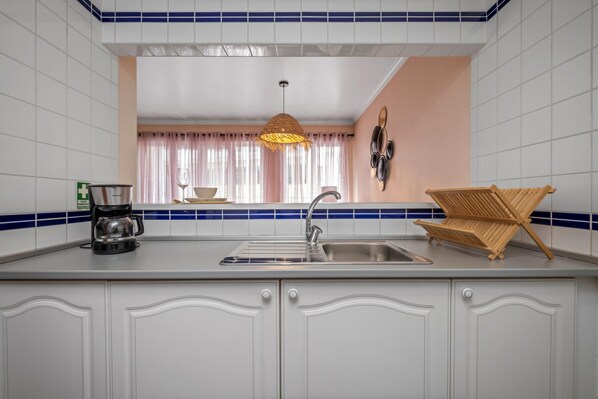 Una cocina con armarios blancos, un fregadero, una cafetera y una lámpara colgante.