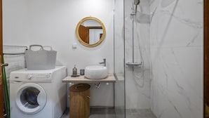 Een kleine badkamer met een wasmachine, een wastafel, een spiegel en een douche.