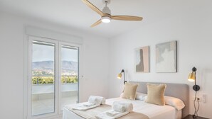Une chambre à coucher comprenant un lit, une table de chevet, un ventilateur de plafond et une vue sur les montagnes, visible à travers une porte coulissante.