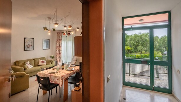 A dining area with a table set for four, a sofa, and a view of a garden through a green door. - Pink apartment 4 minutes walk from free beach (San Vincenzo)