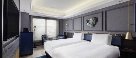 A modern hotel room with a large bed, a desk, a chair, and a TV.