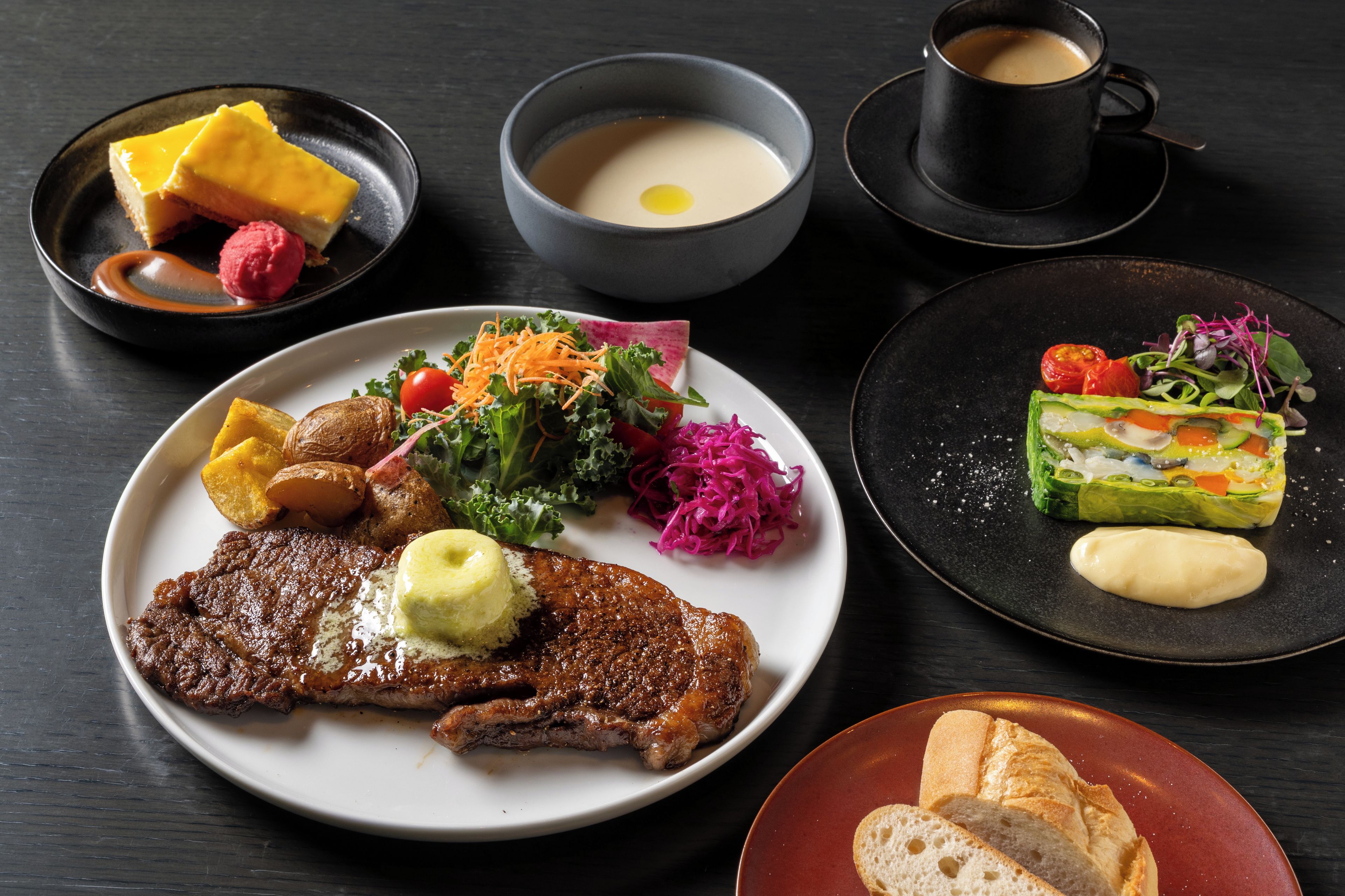 Diversos pratos, incluindo bife, salada e sobremesa, sobre uma mesa escura.