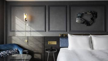 A modern hotel room with a bed, a small round table, a blue sofa, and a wall-mounted lamp.