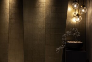 A wall with vertical wooden panels and a bonsai tree on a pedestal.