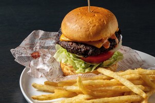 Una hamburguesa con lechuga, tomate y queso en un pan, acompañada de papas fritas en un plato.