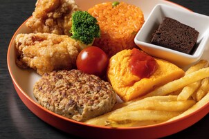 Un plato de comida con pollo frito, una hamburguesa, papas fritas, tomate, una rebanada de queso con kétchup, pan y un pequeño tazón de pastel de chocolate.