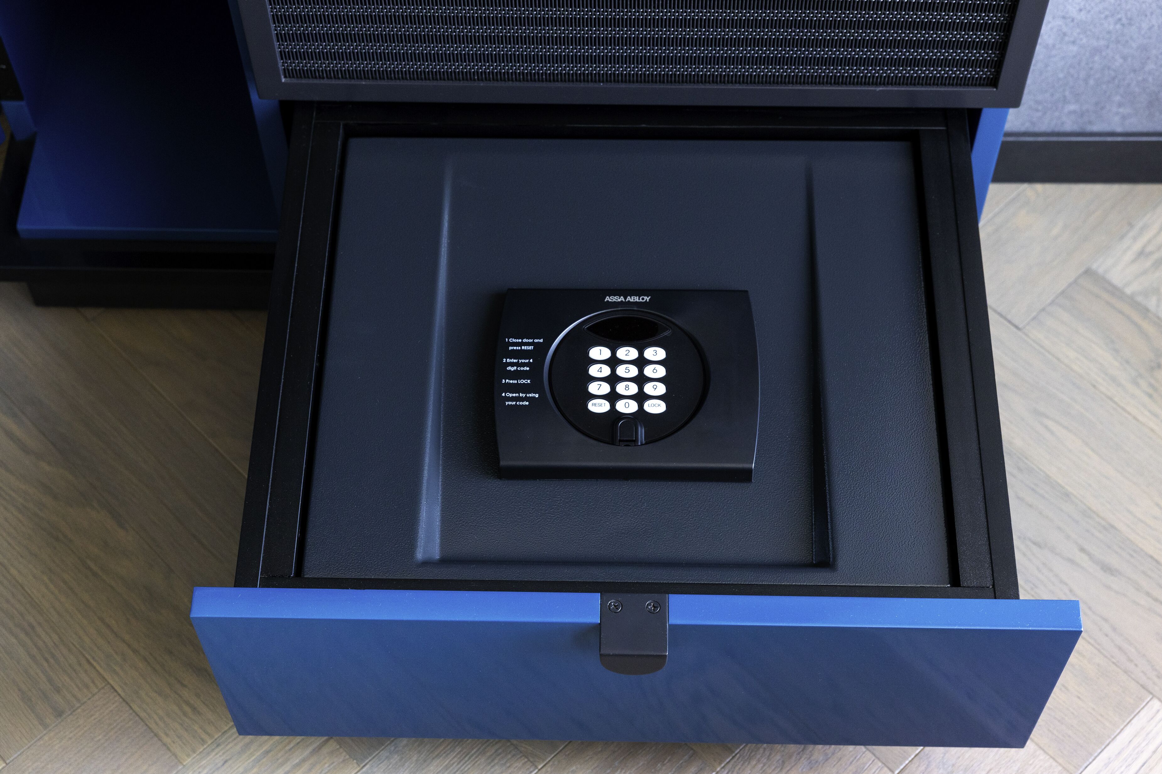 Un coffre-fort noir doté d’un clavier et d’un mécanisme de verrouillage, situé à l’intérieur d’un tiroir bleu.