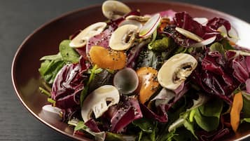 Un tazón de ensalada con diversas verduras de hoja, champiñones y rábanos.
