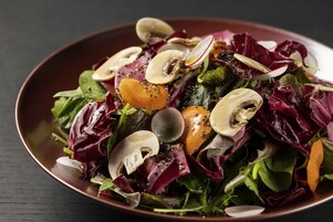 A bowl of salad with various greens, mushrooms, and radishes.