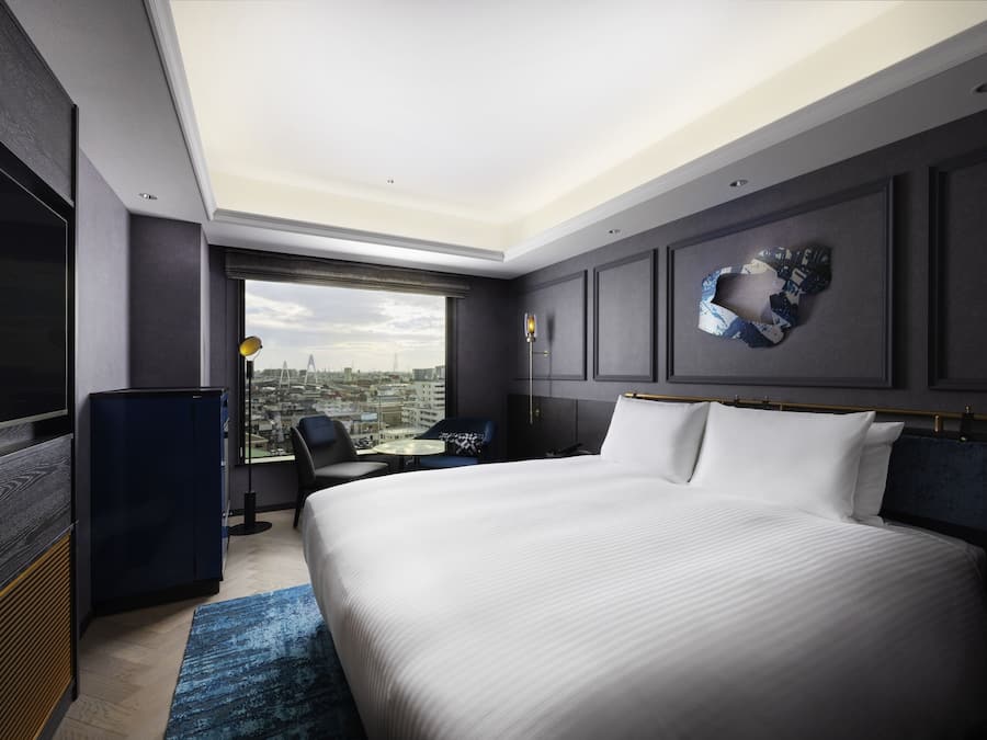 A modern hotel room with a large bed, a desk, and a view of the city.