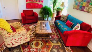A living room with a red sofa, a red armchair, a patterned armchair, a coffee table, and a colorful painting on the wall.