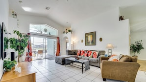 A spacious living room with a large window, a sofa set, a coffee table, and a wooden side table. - 4 Mi to Disney: Family Getaway w/ Game Room! (Kissimmee)