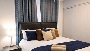 A neatly made bed with a dark headboard, multiple pillows in various colors, a bedside lamp, and a dark blue throw blanket. - Modern and huge soundproof apt w/AC. Steps to Lleras/Provenza in el Poblado. (Medellín)