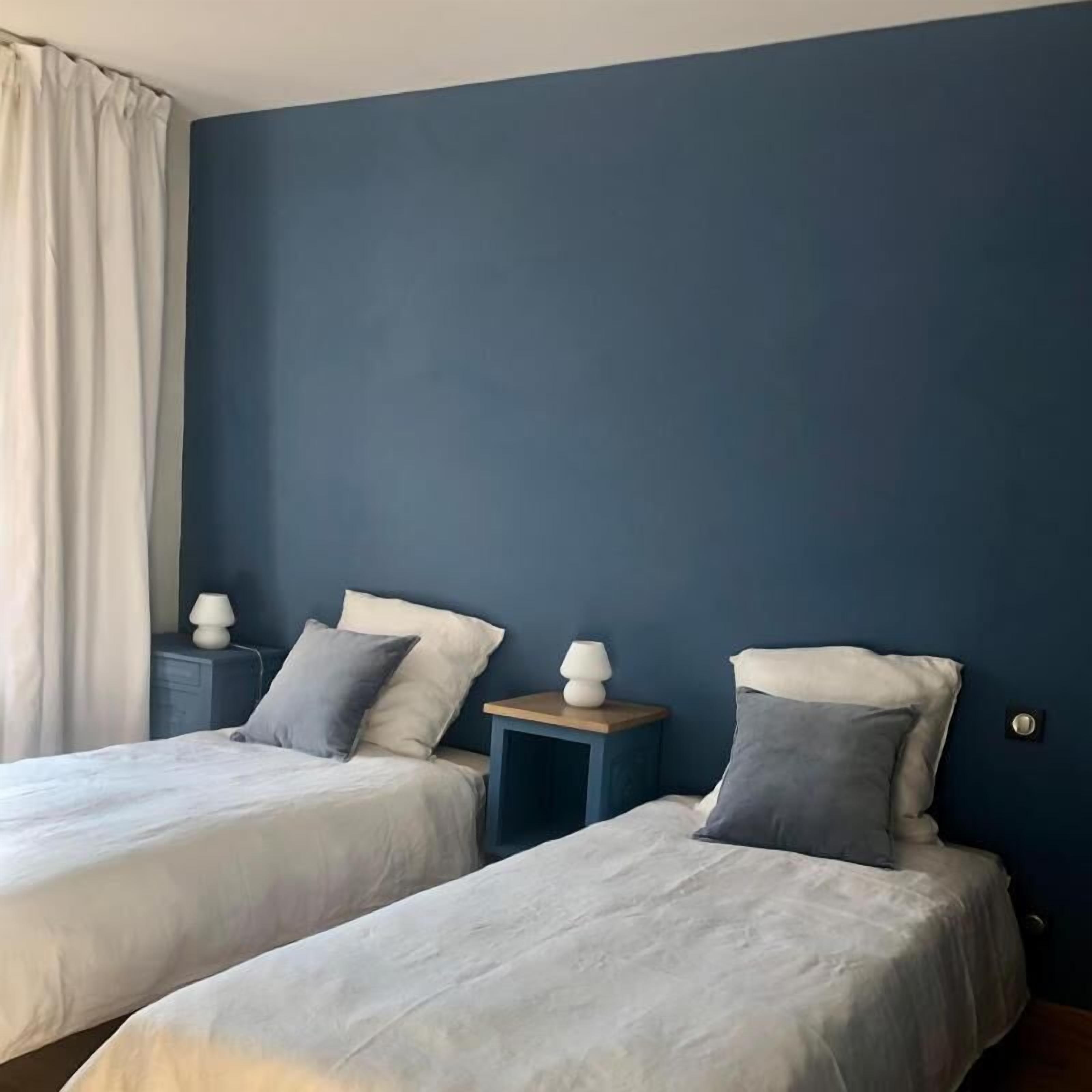 A room with two beds, each with a pillow and a bedside table with a lamp.