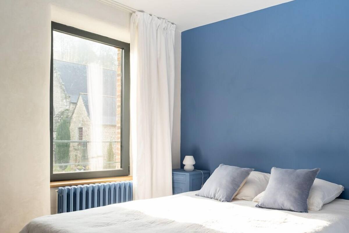 Un dormitorio con una cama grande, una ventana con cortinas, una pared azul y un radiador blanco.