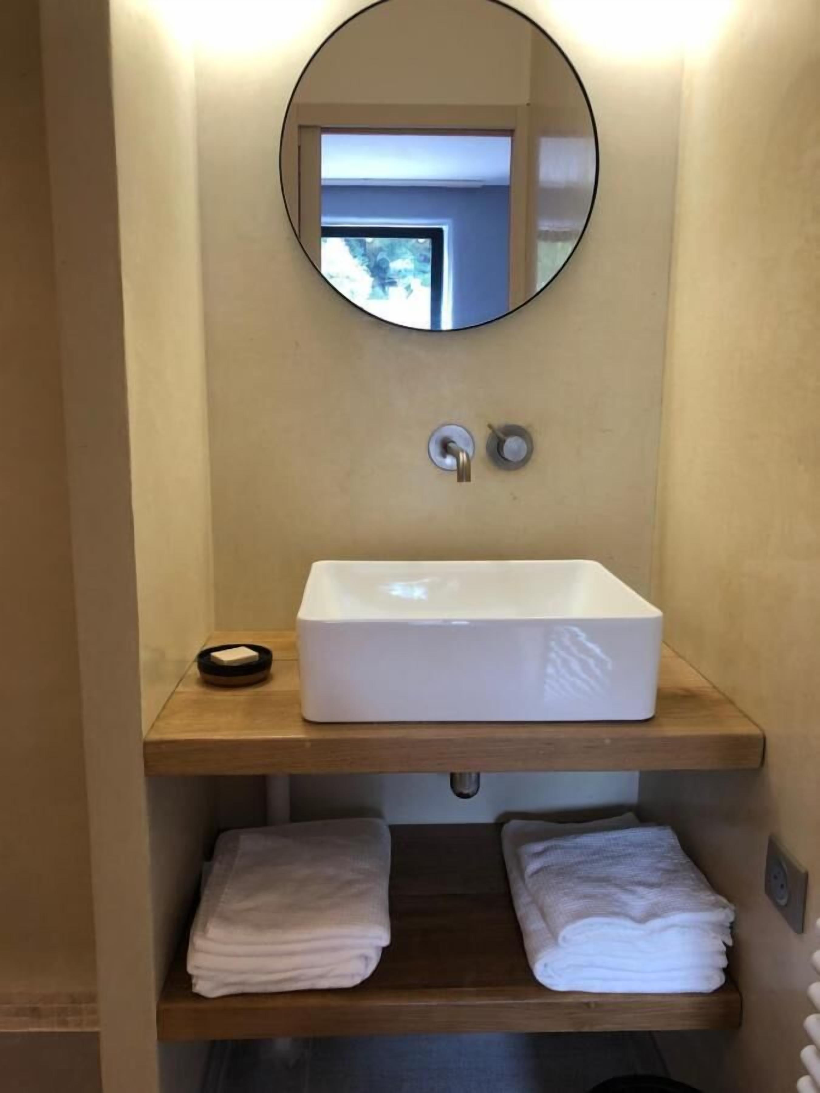 A bathroom with a white sink, a round mirror, and two towel racks with folded towels.