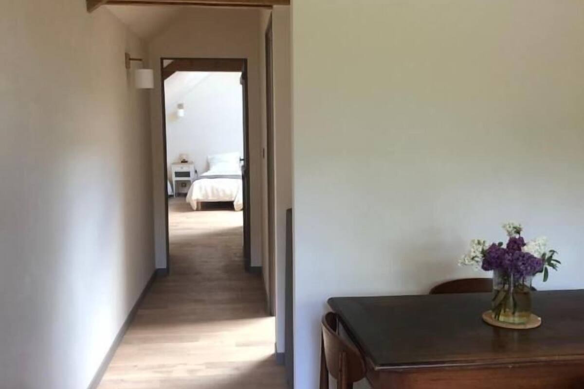 Un comedor con una mesa y sillas de madera, un jarrón con flores y un pasillo que conduce a un dormitorio.