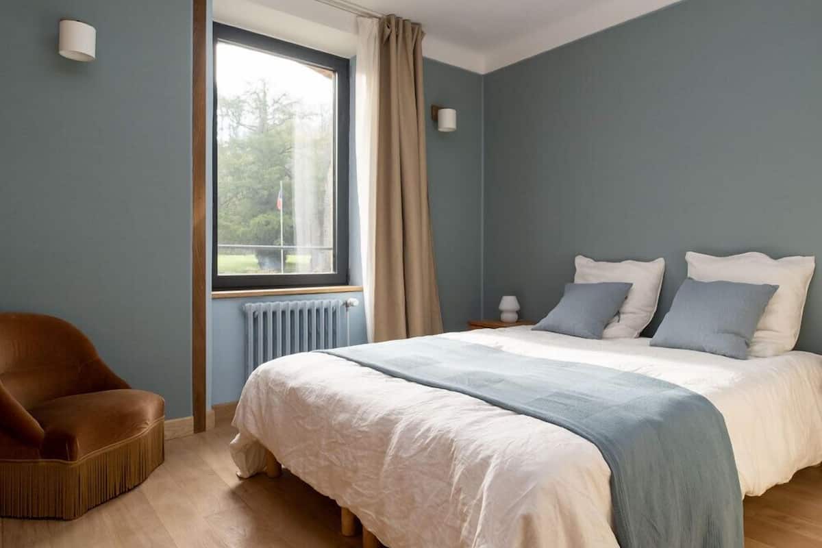Un dormitorio con una cama grande, una silla, una ventana con cortinas y un radiador.