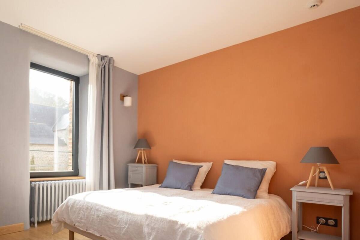 Un dormitorio con una cama grande, dos mesitas de noche, una ventana con cortinas y un radiador.