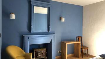 A room with a blue wall, a fireplace, a yellow armchair, a wooden table, and a wooden chair.