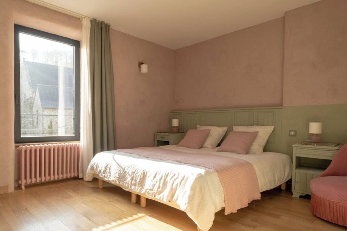 Un dormitorio con una cama grande, una ventana con cortinas, un radiador y una mesita de noche con una lámpara.