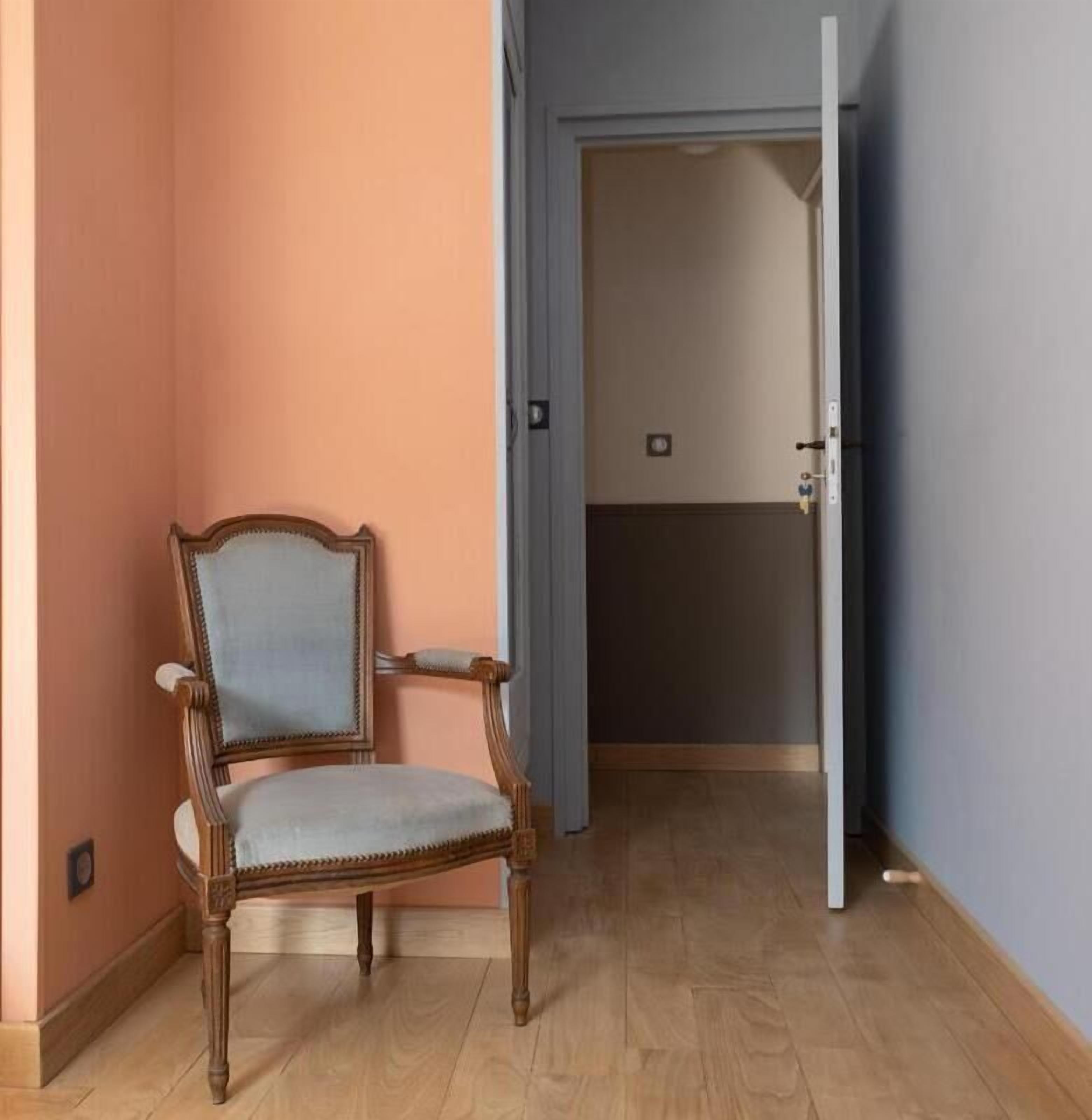 Habitación de esquina con una silla de madera, una puerta que da a otra estancia y suelo de madera.