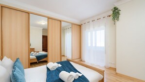 A hotel room with a large bed, a wardrobe, a mirror, and a window with curtains. - Comfy 4BDR Apartment in Portimão by LovelyStay (Portimão)