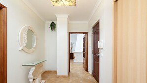 A hallway with a marble floor, a glass console table, a round mirror, and a wooden door. - Comfy 4BDR Apartment in Portimão by LovelyStay (Portimão)