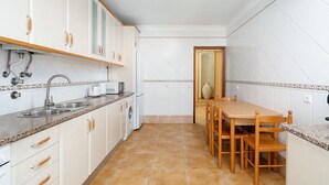 A compact kitchen with white cabinets, a granite countertop, a sink, a toaster, and a wooden dining table with chairs. - Comfy 4BDR Apartment in Portimão by LovelyStay (Portimão)