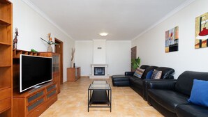 A living room with a flat-screen TV, a fireplace, a black leather sofa, and a wooden entertainment unit. - Comfy 4BDR Apartment in Portimão by LovelyStay (Portimão)