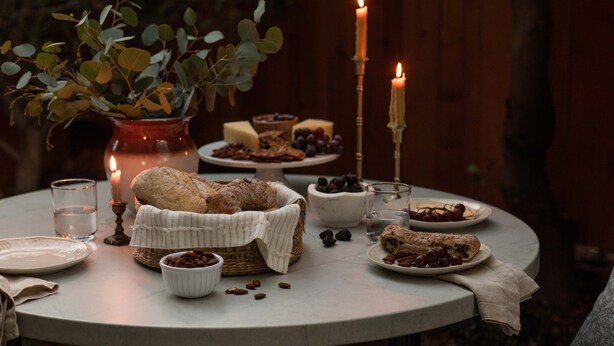 Ein runder Tisch mit einem Brotkorb, einer Vase mit grünen Blättern und Kerzen.