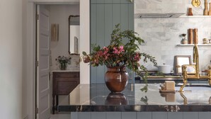 Eine moderne Küche mit Marmorarbeitsplatte, zwei Barhocker, einer Hängelampe und einer Vase mit Blumen.