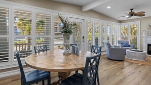 A spacious room with a large wooden dining table, blue chairs, a round coffee table, and a ceiling fan.