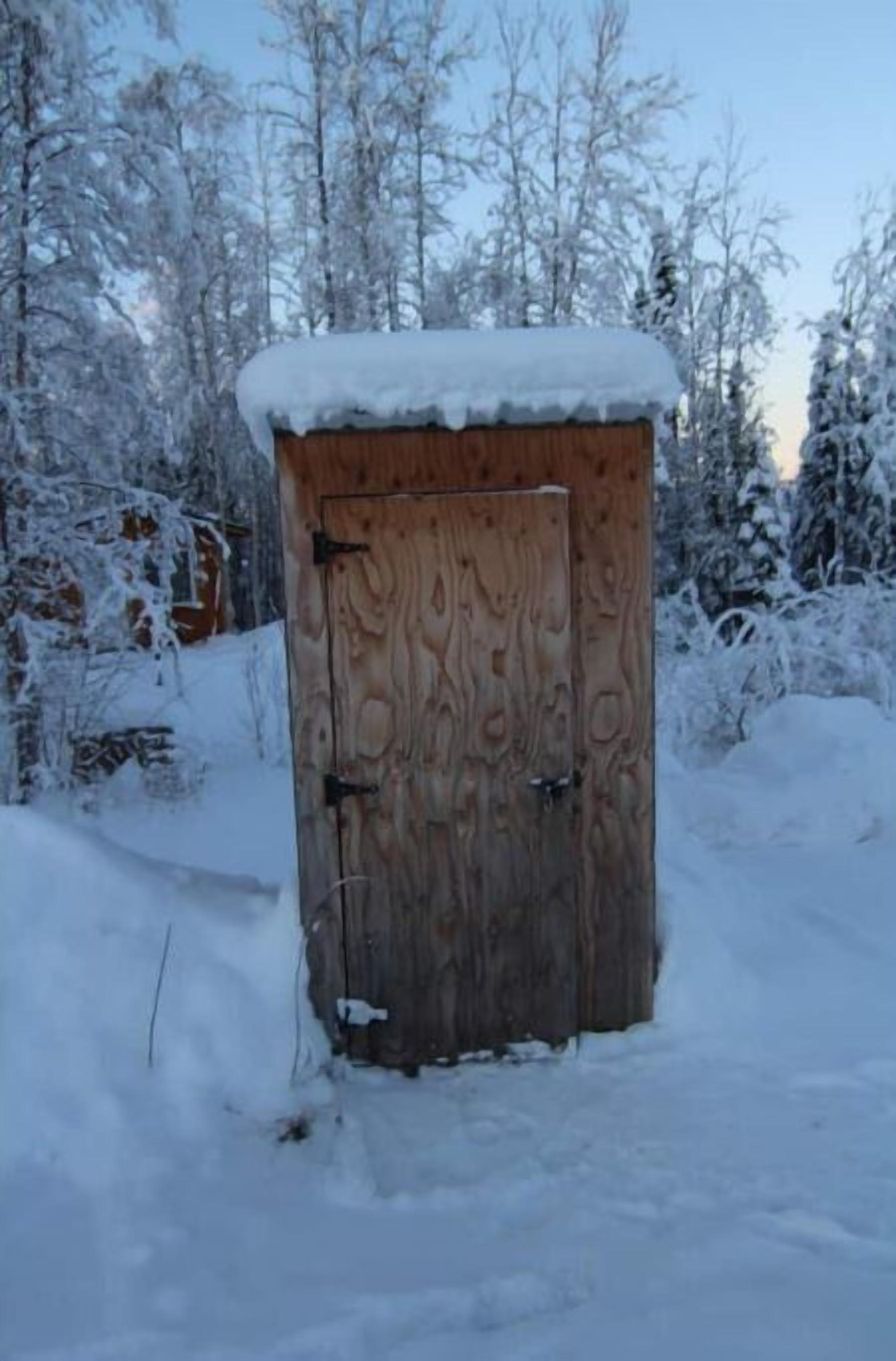 Una cabaña de madera con techo nevado, rodeada de árboles cubiertos de nieve.