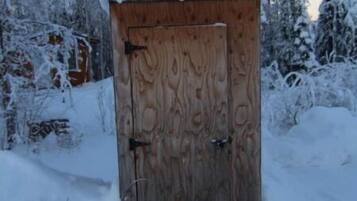 Una cabaña de madera con techo nevado, rodeada de árboles cubiertos de nieve.
