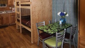 Een houten blokhut van binnen met stapelbedden, een eettafel met stoelen en een keukenhoek.