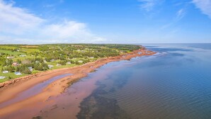 An aerial view of a coastal area with houses, a beach, and a forested landscape.