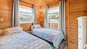 A wooden-paneled room with two beds, a nightstand, a dresser, and a chandelier.